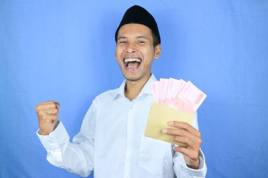 Asyalı Müslüman adamın elinde para tutmasının mutlu ifadesi. Rupiah banknotları beyaz arka planda izole edilmiş.