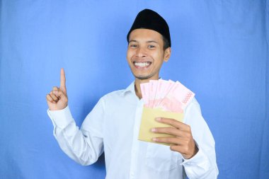 Asyalı Müslüman adamın elinde para tutmasının mutlu ifadesi. Rupiah banknotları beyaz arka planda izole edilmiş.