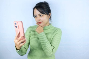 Beyaz arka planda akıllı telefon tutan Asyalı kadının düşünceli ifadesi