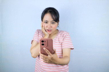 Asyalı kadının beyaz arka planda akıllı telefondan mesaj okuması şok edici bir ifade.