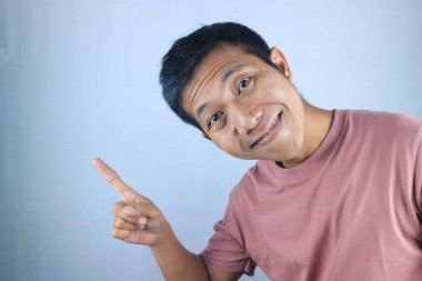 Gülen Asyalı genç adamın sağ tarafı göstermesi ve beyaz arka planda izole edilmiş ürünleri tanıtması komik bir yüz ifadesi.