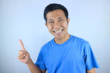 Yan tarafı gösteren gülümseyen Asyalı genç adamın komik yüz ifadesi beyaz arka planda izole edilmiş ürünü tanıtıyor.