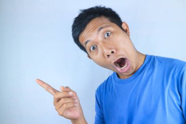 Beyaz arka planda izole edilmiş ürünleri destekleyen Asyalı genç adamın komik yüz ifadesi.