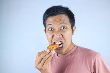 Beyaz arka planda izole edilmiş, elinde patates kızartması tutan Asyalı genç adamın komik ifadesi.