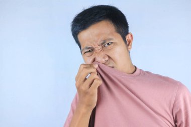 Asyalı adam kendi kokusunu kontrol eder, ıslak koltuk altını koklar ya da terler, beyaz arka planda izole olur.