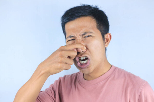 funny expression of young asian man covering his nose because of disgusting smell