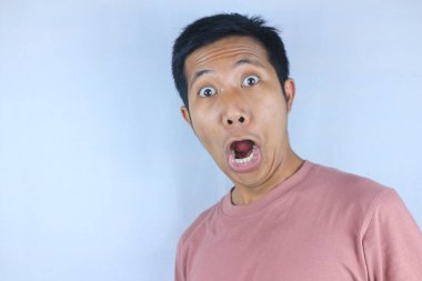 Komik yüz ifadesi genç Asyalı adam beyaz arka planda izole edilmiş kameraya bakarken şok oldu.