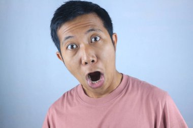 Komik yüz ifadesi genç Asyalı adam beyaz arka planda izole edilmiş kameraya bakarken şok oldu.