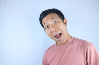 Komik yüz ifadesi genç Asyalı adam beyaz arka planda izole edilmiş kameraya bakarken şok oldu.