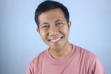 Gülümseyen yüz ifadesi genç Asyalı adam kameraya bakarken mutlu, beyaz arka planda soyutlanmış.