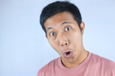 Aptal yüz ifadesi. Genç Asyalı bir adam beyaz arka planda izole edilmiş kameraya bakıyor.