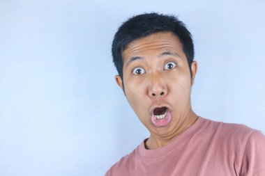 Komik yüz ifadesi genç Asyalı adam beyaz arka planda izole edilmiş kameraya bakarken şok oldu.