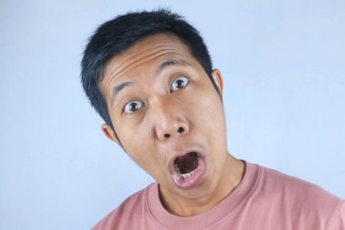 Komik yüz ifadesi genç Asyalı adam beyaz arka planda izole edilmiş kameraya bakarken şok oldu.