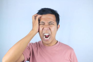 Kafasını tutarken beyaz arka planda izole edilmiş Asyalı genç adamın stresli yüz ifadesi.