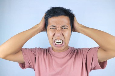 Kafasını tutarken beyaz arka planda izole edilmiş Asyalı genç adamın stresli yüz ifadesi.