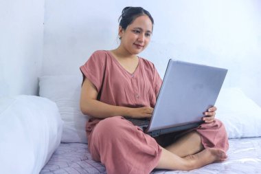 Genç kız laptopta yatakta çalışıyor. İş kadını, teknoloji kavramı. Evden çalış.