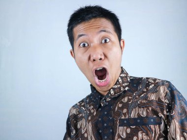 Vay canına, şaşırmış surat ifadesi. Batik kıyafetler giyen Asyalı adam kameraya bakıyor.