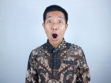 Vay canına, şaşırmış surat ifadesi. Batik kıyafetler giyen Asyalı adam kameraya bakıyor.