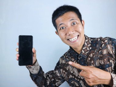 Batik giysili gülümseyen Asyalı adam boş ekranlı akıllı telefonu gösteriyor. beyaz arkaplan