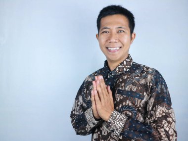 Batik giysiler giymiş Asyalı bir adamın gülümseyen yüz ifadesi. Kameraya bakıp selam veriyor.