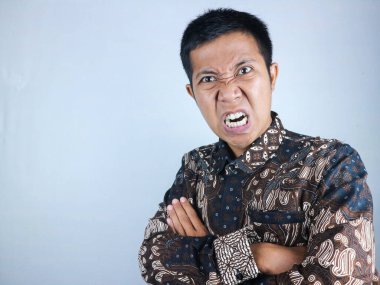 Asyalı bir adamın kolları kameraya çaprazken batik kıyafetler giymesi.