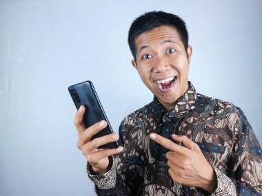 Batik giysili gülümseyen Asyalı adam boş ekranlı akıllı telefonu gösteriyor. beyaz arkaplan