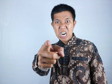 Kamerayı işaret ederken batik kıyafetler giyen Asyalı adamın kızgın yüz ifadesi.