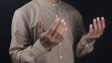 Kahverengi gömlek giyen bir iş adamı. Siyah bir arkaplanda dua eden el hareketlerini gösteriyor.