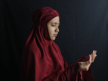 Mukena giyen müslüman bir kadının dua ederken elinde boncuklar tutarken yan görüntüsü