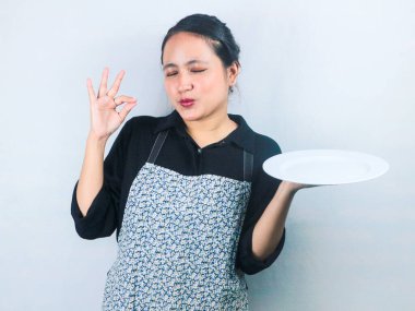 Önlüklü güzel Asyalı kadın beyaz arka planda boş beyaz tabak ya da tencere tutuyor.