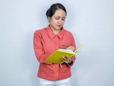 Güzel Asyalı kadın kitap planlayıcısını beyaz arka planda izole edilmiş notlar yazarken yakaladı.