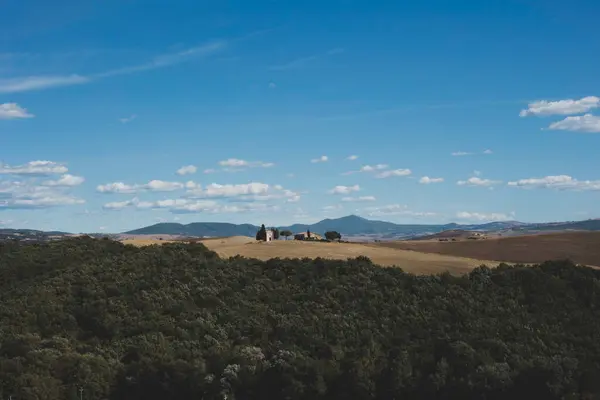 Fotoğrafta yeşillik ve açık alanlarla kaplı yuvarlanan tepelerle manzaralı bir manzara resmediyor. Uzakta, küçük bir kilise ya da ev bir tepenin tepesinde tek başına duran birkaç ağacın arasına kurulur..