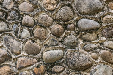 Textured stone wall made with rounded rocks tightly packed together, showing rough surfaces and earthy tones.