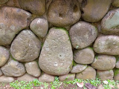 A rustic stone wall built with large rounded stones. The surface shows moss and natural textures, creating an earthy and organic appearance.