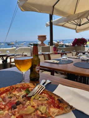 Yaz tatilinde deniz manzaralı İtalyan pizzası ve bira.