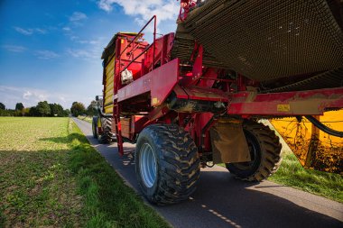 Kırsal yolda tarla arazisi yakınlarında kırmızı tarımsal hasat makinesi