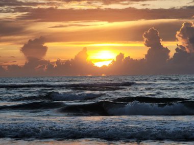 Rolling waves of the Atlantic Ocean with the yellow sun peeking through disappearing storm clouds