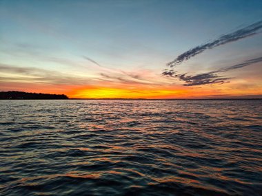 Sersemletici bir gün batımı manzarası, turuncu ve mavi renkli canlı renklerin su yüzeyinden yansıması, resim gibi ve huzurlu bir ortam yaratıyor..