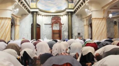 Bir camide cemaat içinde namaz kılma sürecini yetişkinler ve çocuklar takip ediyor..