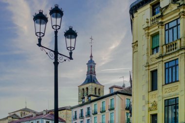 Looking up at the roofs of historical buildings from Plaza Mayor with a lamp post in the foreground, in Segovia, Spain.