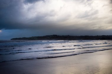 Gijon Körfezi 'nin genel bir silueti. Akşamları sahilde dramatik bir gökyüzü ile dalgalar yükseliyor..
