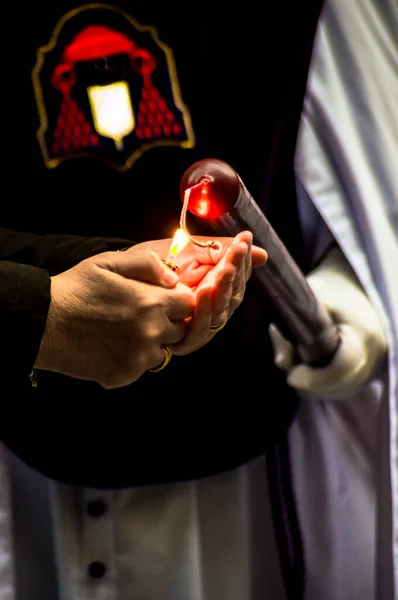 宗教行事の際に手袋をはめた手で持つ宗教的なスタイルの長い赤いキャンドルを照らす手のペアのビュー — ストック写真