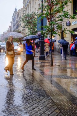 Sol 'da iki kadın şemsiyeyle karşıdan karşıya geçiyor. Fırtına Aline, Madrid 'in merkezinden ayrılan sonbahar sezonundaki ilk şiddetli yağmuru getirdi. Herkes daha sıcak kıyafetler ve şemsiyelerle Madrid İspanya' ya uzandı. Madrid Spai