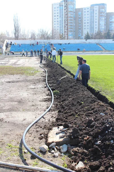 people doing general cleaning and digging in unity and collaboration a trench in a stadium for aqueduct and lawn irrigation
