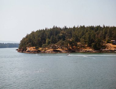 GEORJİK, BC, CANADA - 14 Ağustos 2024: motorlu tekne parlak bir gökyüzünün altındaki berrak sularda huzur içinde yüzüyor