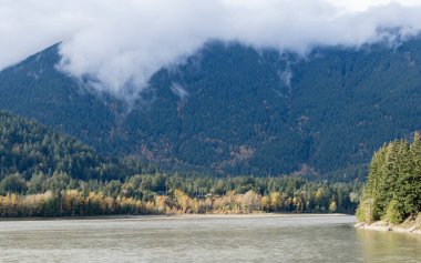 UMUT, BC, CANADA - 21 Ekim 2024: Dağlar ve bulutlarla dolu bir Fraser nehri ve ormanın güzel sonbahar manzarası. Manzaralı kırsal alan. Sonbahar doğası