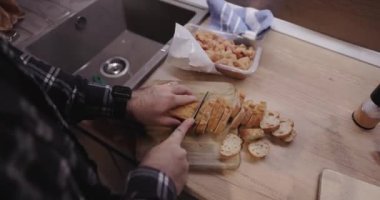 Ekmeği bruschetta için dilimleyen yetenekli bir adam mutfak uzmanlığını sergiliyor. Elleri ekmeği zarifçe tutuyor, ince ve düzgün dilimler oluşturuyor..