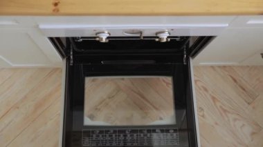 Young woman takes out a freshly cooked delicious pizza from the oven, top view, close up. Homemade pizza cooked in a white oven in a light spacious Scandinavian style white kitchen.