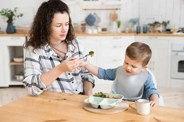 可爱的幼儿男孩拒绝吃他妈妈给他的蔬菜 一位年轻的母亲担心她的儿子不想吃蔬菜 于是试图说服他吃一块西兰花 — 图库照片