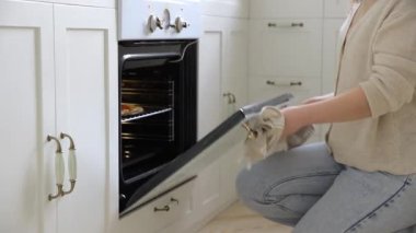 Genç kadın fırından yeni pişmiş lezzetli bir pizza çıkarıyor ve aromasının tadını çıkarıyor. İskandinav tarzı beyaz bir mutfakta beyaz bir fırında ev yapımı pizza..